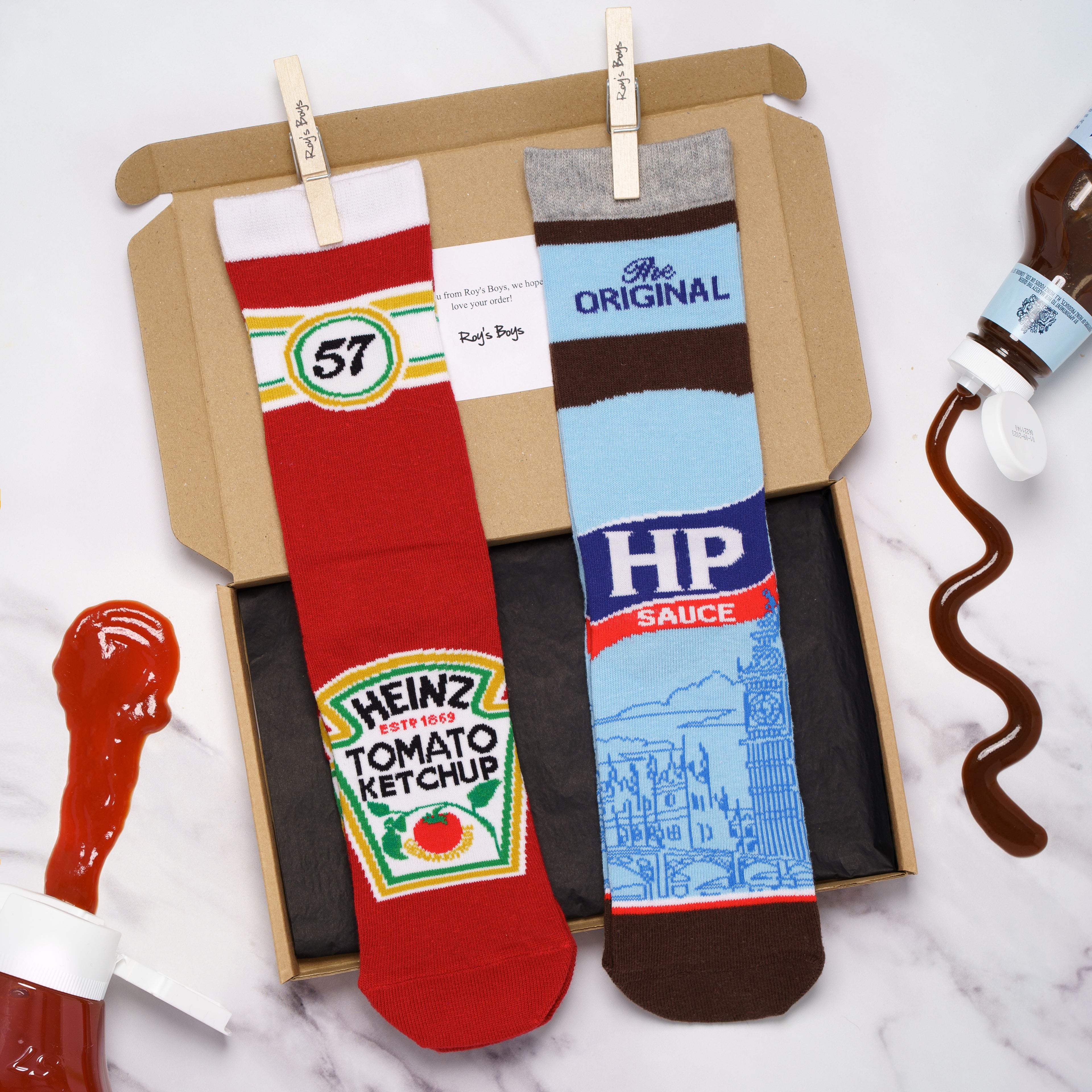 A cardboard presentation gift box displaying red Heinz Tomato Ketchup socks and light blue HP Sauce socks alongside stylized condiment splashes