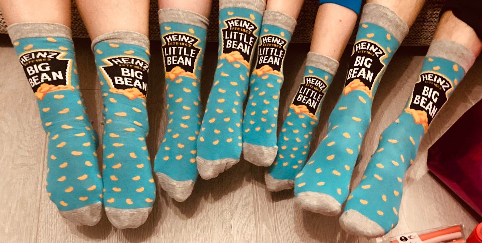 A family of four wearing matching blue Heinz Baked Beans novelty socks, featuring the Big Bean and Little Bean designs