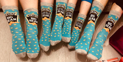 A family of four wearing matching blue Heinz Baked Beans novelty socks, featuring the Big Bean and Little Bean designs