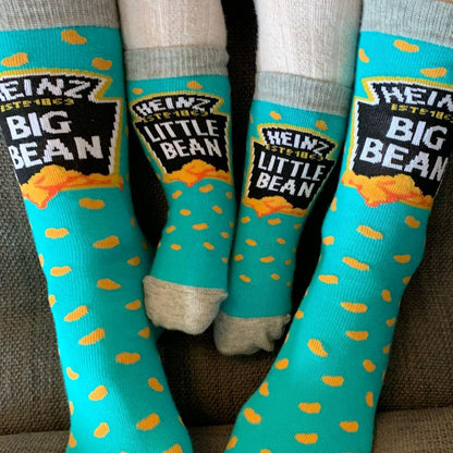 An adult and a child wearing matching blue Heinz Baked Beans novelty socks featuring the Big Bean and Little Bean logos